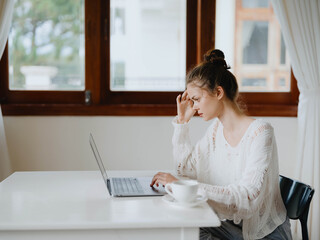 Creative young woman working at a desk at home in a cozy interior with a cup of drink, home office freelancer with a smile, communication and education online