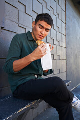 Young man eating flaky pastry by gray geometric brick wall