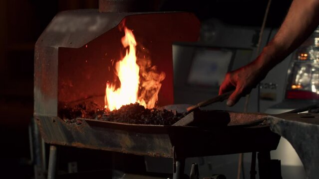 Blacksmith hand forging hot metal on an anvil in forge with spark fireworks
