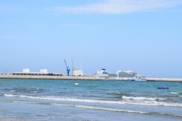 Coastal port scene with cruise ships, industrial cranes, blue sky, gentle sea waves, harbor infrastructure, maritime travel, waterfront, summer atmosphere, transportation, holiday, tourism,