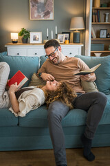 man and woman caucasian adult couple read books at home on sofa bed
