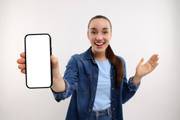 Surprised young woman showing smartphone in hand on white background, selective focus. Mockup for...