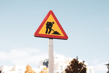 Roadworks yellow red triangular sign on a city street against blue sky. Temporary construction icon...