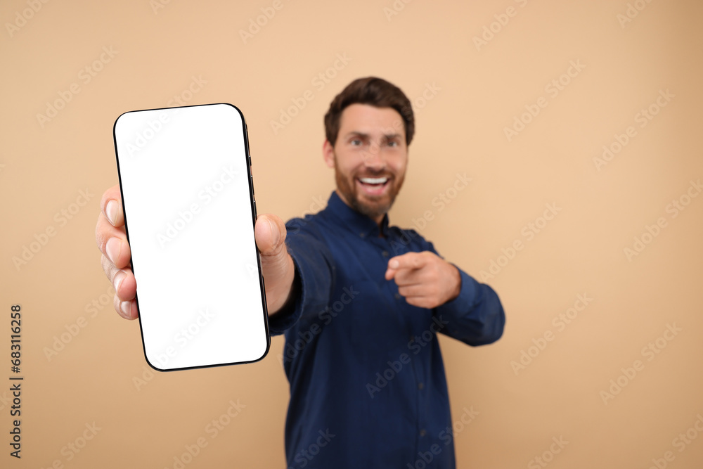 Poster handsome man showing smartphone in hand and pointing at it on light brown background, selective focu