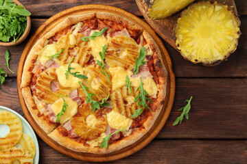 Delicious pineapple pizza and ingredients on wooden table, flat lay
