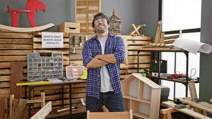 Portrait of a smiling young man carpenter, striking a confident pose with arms crossed at carpentry workshop, wearing glasses and showcasing his woodwork skills