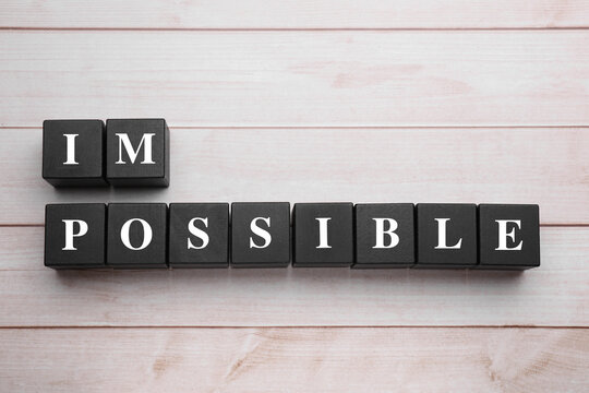 Motivation concept. Changing word from Impossible into Possible by removing black cubes on light wooden table, flat lay