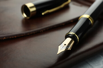 Stylish fountain pen, cap and leather notebook on grey table, closeup