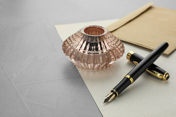 Stylish fountain pen, inkwell, envelope and paper on grey textured table, space for text