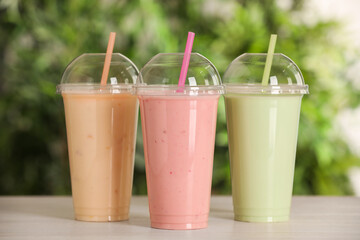 Plastic cups with different tasty smoothies on wooden table outdoors