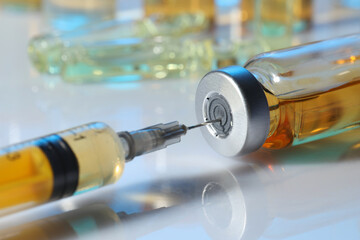 Filling syringe with orange medication from glass vial on white table, closeup