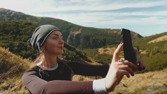 Woman making selfie in Carpathian mountains hiking tour. Tourist female take photo with smartphone, sharing nature beauty landscape. Traveler spending vacation outdoors, trekking, sports. Slow motion