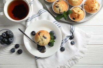 Delicious sweet muffins with blueberries and mint served on white wooden table, flat lay