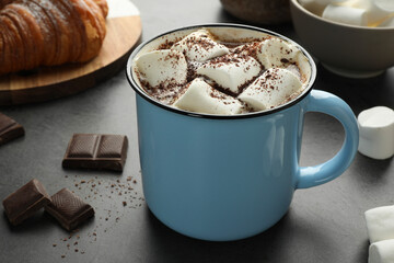 Delicious hot chocolate with marshmallows, cocoa powder and spoon on grey table, closeup