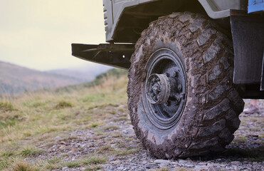 Fototapeta na wymiar Wheel closeup in a countryside landscape with a mud road. Off-road 4x4 suv automobile with ditry body after drive in muddy road area
