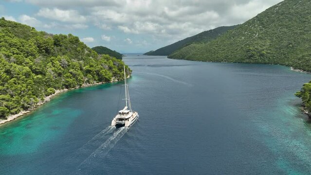 Big catamaran sails out of the Mljetski canal on a sunny day. Drone panning shot