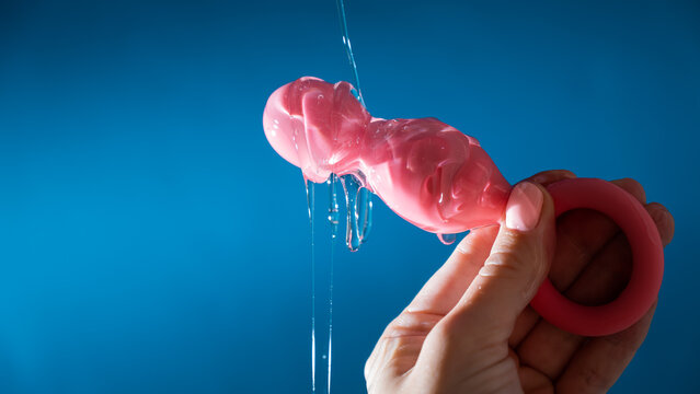 Woman pouring lubricant on pink anal beads on blue background. 