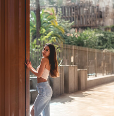 Urban vibes: stylish latino girl in jeans and little top posing against copper wall under sunlight, with big copy space