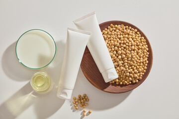 Two unlabeled tubes decorated with a dish of soybean seeds, a petri dish of soybean milk and a jar filled with oil. Mockup of skin care cosmetic tube of beauty facial