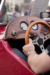Vertical photo. Male hand on wooden brown steering wheel. Man driving classic vintage old retro red...