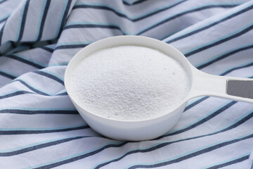 Detergent powder in measuring spoon on cloth before washing. Laundry concept.