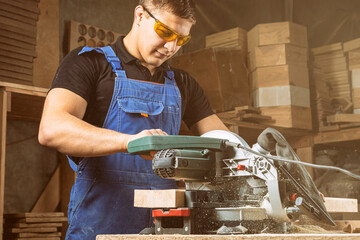 Close-up as a young male construction worker carpenter saws a circular saw blade, sawdust fly in...
