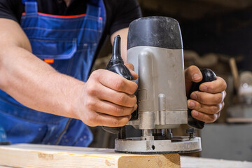 Young man by profession carpenter builder equals a wooden milling machine on a wooden table in the workshop