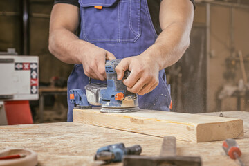 Young man carpenter grinding wood with sandpaper in carpentry or diy workshop. Electric sander working in carpentry