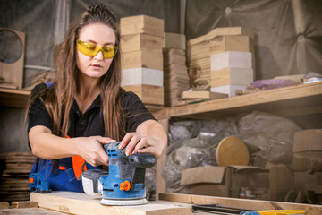 Close up of an young woman builder carpenter equals polishes wooden board with a polishing machine...