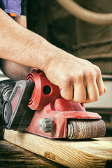 Close-up hand of an man carpenter  sanding plank to smooth with an electric sander machine  in...