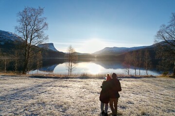 A couple stands together, basking in the sunrise over a frosty Norwegian lake