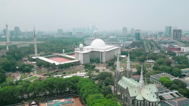 Cinematic aerial view of the iconic Istiqlal Mosque near the Jakarta National Monument or Monas and the Cathedral Church.