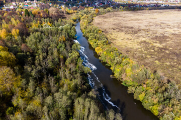 Aerial view of a picturesque autumn landscape with a river separating the forest and field