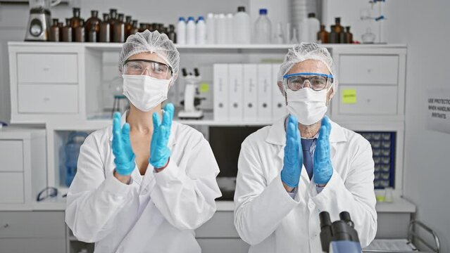 Two zealous scientists in medical masks and gloves applauding breakthrough in corona research at indoor lab