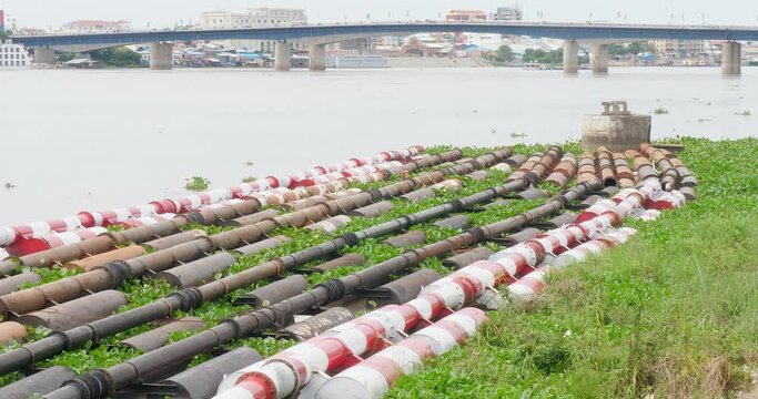 row of water pipes running  parallel to the riverbank. The pipes are used to transport water from the river to a town.