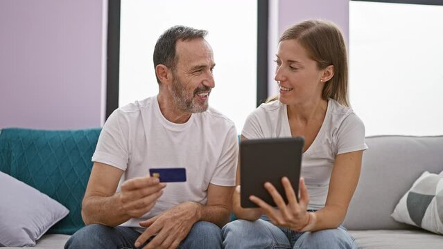 Father and daughter using touchpad and credit card sitting on sofa smiling at home