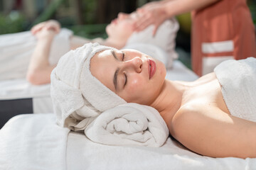 Relaxed young woman lying on massage table with eyes closed in spa salon