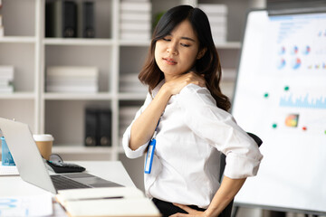 Asian woman working hard in the office having aches and pains in her torso and shoulders.