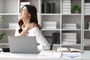 Asian woman working hard in the office having aches and pains in her torso and shoulders. - obrazy, fototapety, plakaty