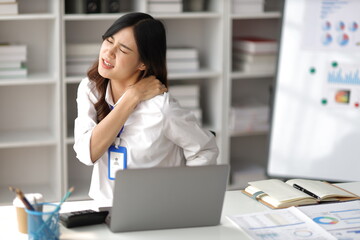 Asian woman working hard in the office having aches and pains in her torso and shoulders.