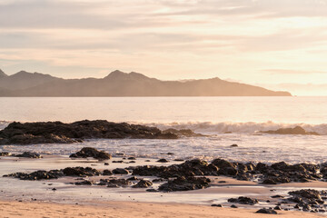 Dusk on the Ocean with a Rocky Beach in the Foreground and hills in the Distance