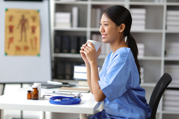 Female doctor in hospital office drinking coffee and stretching relax during break time.