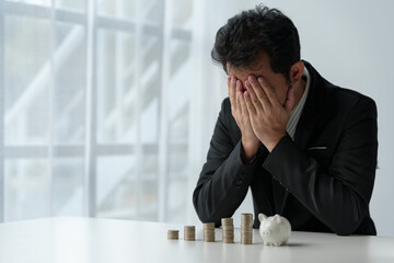Businessman covers his face with his hands against a stack of coins, perspective on planning...