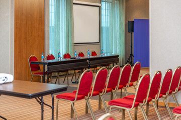 Empty conference room with screen, banner, table and chairs. Business meetings, forums and presentations.