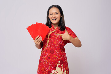 Smiling young Asian woman wearing a traditional cheongsam qipao dress points a finger at angpao or red packet of monetary gifts isolated on white background. Happy Chinese New Year