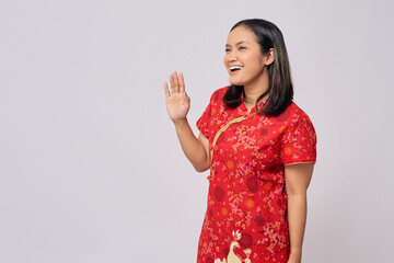 Smiling happy young Asian woman wearing a traditional cheongsam qipao dress waving a hand to a...