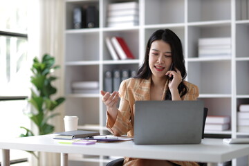 Asian businesswoman working on paperwork in office and calling someone.