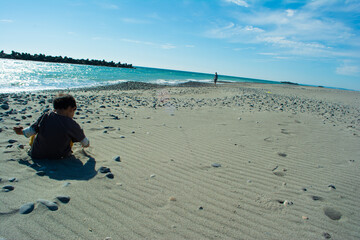 中田島砂丘の砂利で遊ぶ子どもの後ろ姿と青空