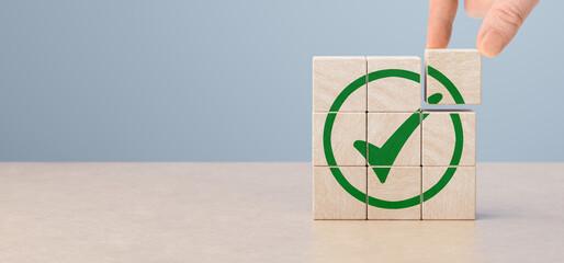 Wooden blocks and green check mark icon with hand on table background. Goals achievement and...