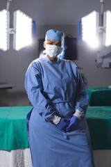 Portrait of biracial female surgeon wearing surgical gown and face mask in operating theatre